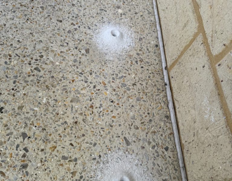 Concrete perimeter drill holes prepared for chemical termite barrier installation around a residential property.