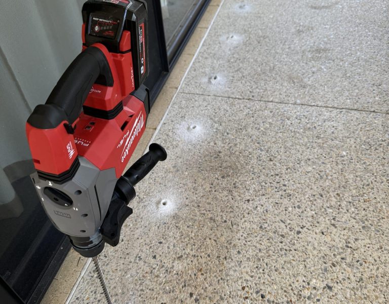 Professional termite treatment technician drilling concrete slab for external chemical termite barrier application.